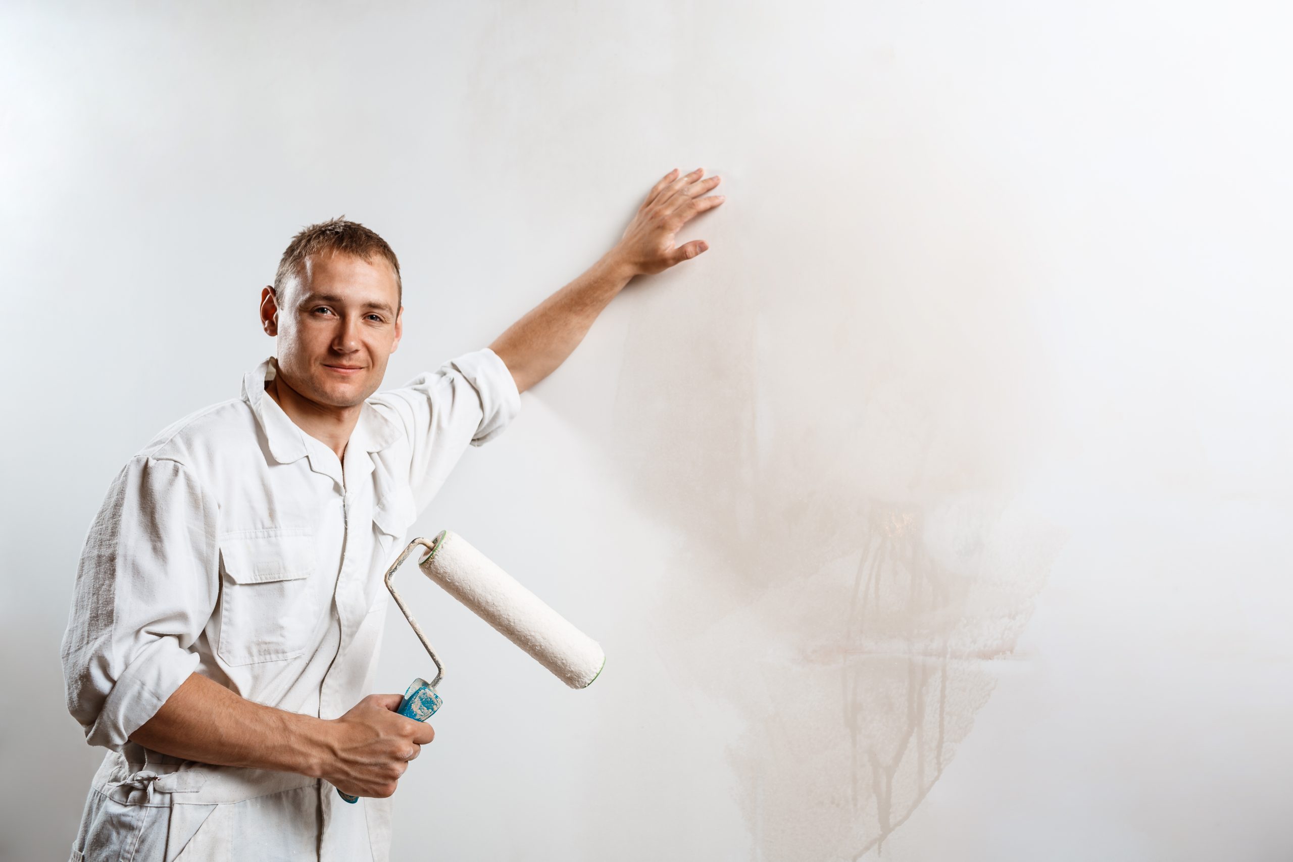Professional worker looking at camera, holding roller over white wall. Copy space.